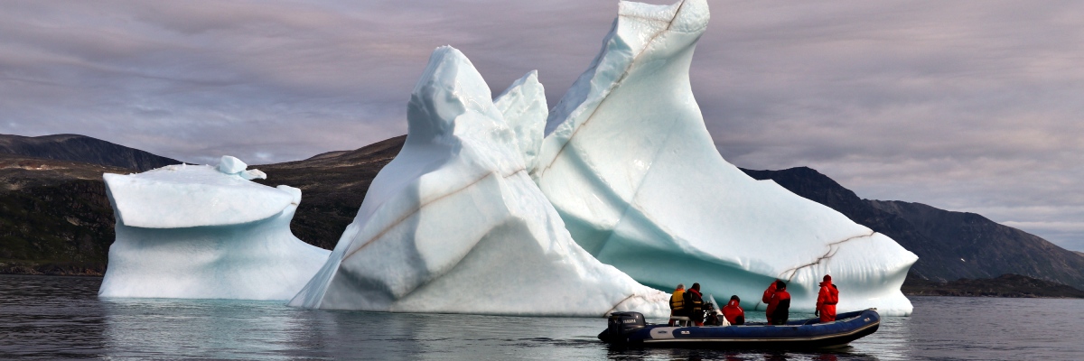 Un bateau pneumatique avec cinq membres d’équipage à bord passe devant un grand iceberg.