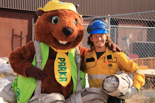 Parka, the Parks Canada mascot, poses with a fire crew member. Both are holding rolled up fire hose, commonly referred to as ‘melons’.