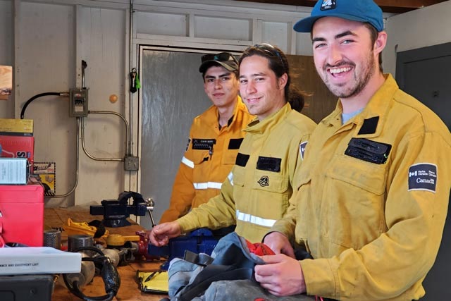 Three fire crew members smile as they prepare their field equipment for the day in Wood Buffalo National Park