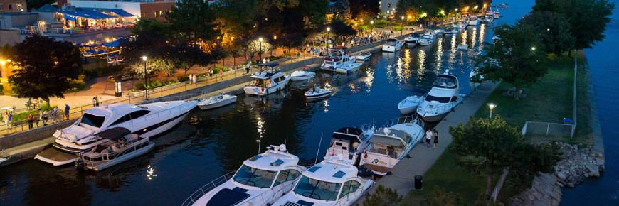 Several boats moored at the Sainte-Anne-de-Bellevue Canal and people walking on the banks at night.
