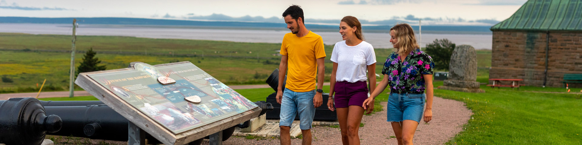 Visitors looking at an interpretation panel outside the fort, with old cannons on display nearby.