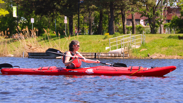 Femme à bord d'un kayak en eau calmes par une journée ensoleillée.