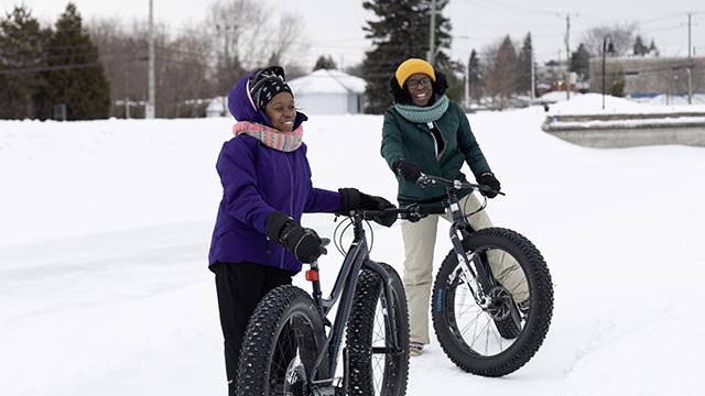 2 smiling women with an oversized bike in winter.