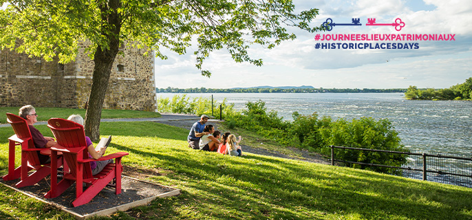 An elderly couple and a family with children lounging in the park beside the Richelieu River and Fort Chambly National Historic Site on a hot summer's day.