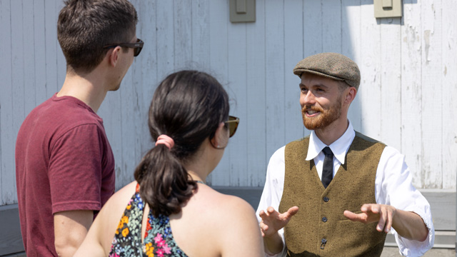Un employé habillé en personnage costumé du début du 20e siècle discute avec un couple de visiteur au lieu historique national de la Grosse-Île-et-le-Mémorial-des-Irlandais.