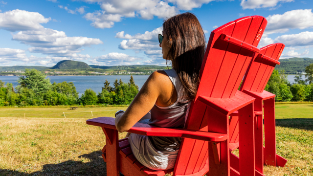 Une femme assise sur une chaise Adirondak rouge regarde une rivière .