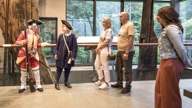 A group of visitors listen to a duo of costumed interpreters impersonating French and English marine captains.