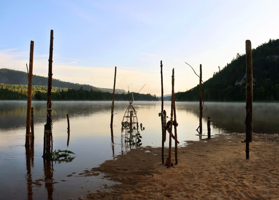 An art and nature installation reflects on the calm surface of a lake.