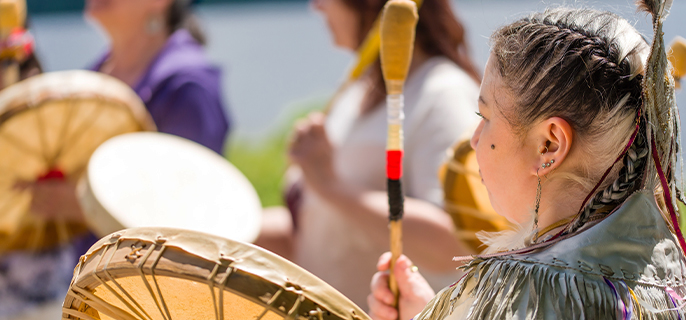 "Une personne autochtone joue du tambour à main avec d'autres membres de sa communauté.”
