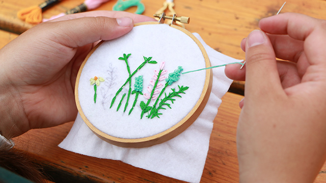 Close-up image of hands with needle and thread working on a floral embroidery design.