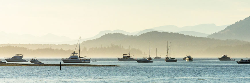 A view across Sidney Channel under the low evening sun, nearby islands silhouetting the boats moored off Sidney Island.
