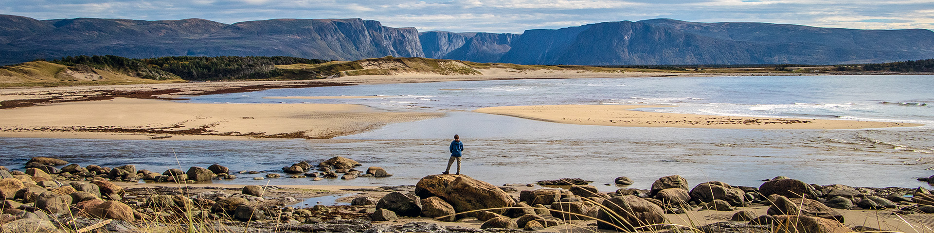 Landscape photo of a person standing in front of Western Brook Pond in Gros Morne National Park