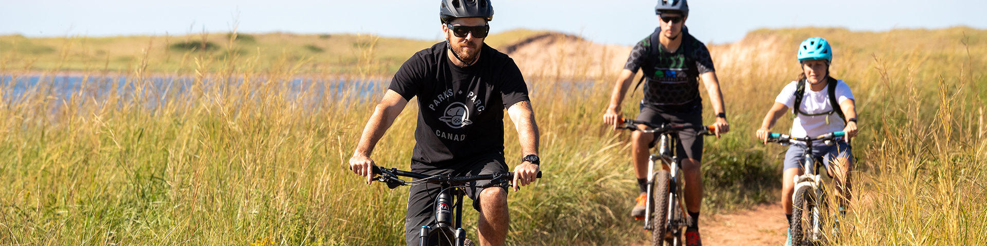 Trois personnes à vélo sur un chemin de terre près des dunes dans le parc national de l'Île-du-Prince-Édouard.