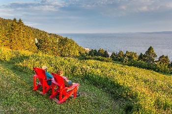 Two persons sitting on red chairs looking at the sea