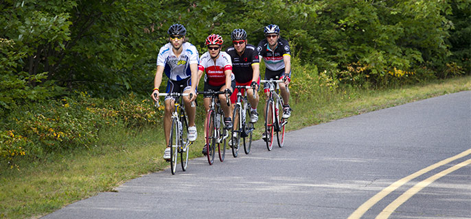 Quatre cyclistes qui roulent sur le bord de la route Promenade avec une forêt en arrière-plan.