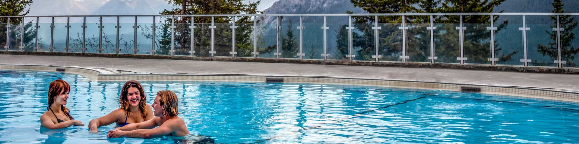 Three persons chatting in the pool with a mountain backdrop at Upper Banff Hot Springs.