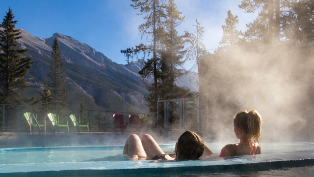 Two people relaxing in the pool with a mountain backdrop at Upper Banff Hot Springs.