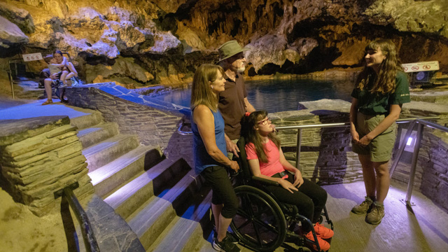 A staff member with family, including a person in a wheelchair, inside the Cave at the Cave and Basin National Historic Site.
