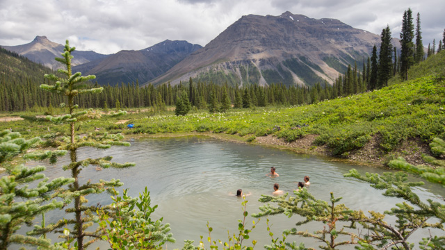 Five people in a natural pool with mountains in the background at Broken Skull Hot Springs in Nááts'įhch'oh National Park Reserve.
