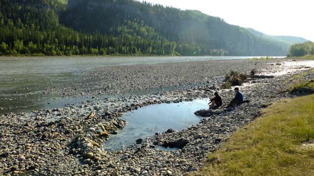 Two visitors next to hot springs along a river in Nahanni National Park Reserve