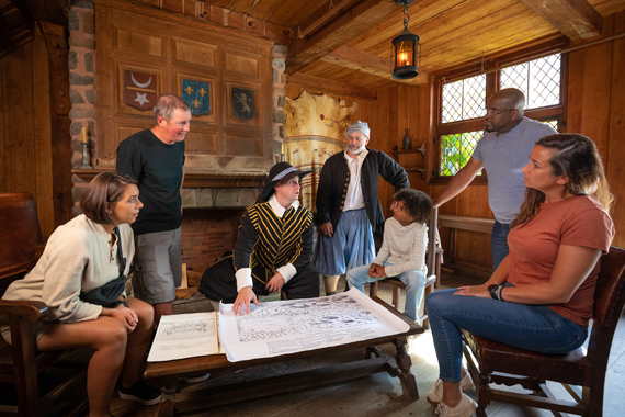 A group of visitors with a costumed interpreter looking at a historic map.