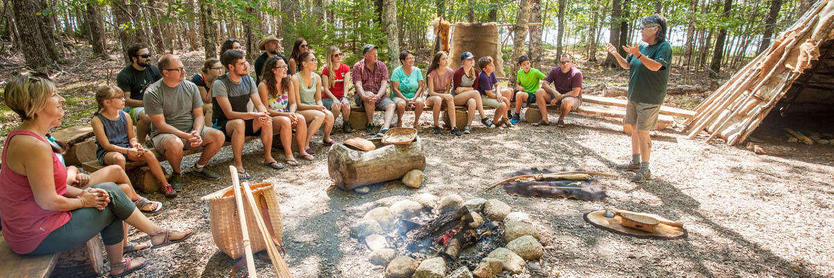 A group of visitors listening to an interpreter around a campfire.