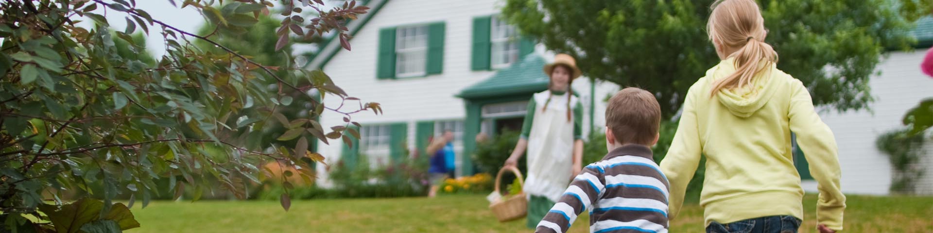 A guide in an Anne Shirley costume with a young girl walk past a historic house. 