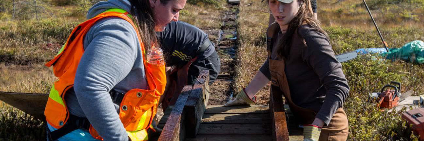 DeuxÂ femmes soulèvent un tronçon d’une promenade en bois.