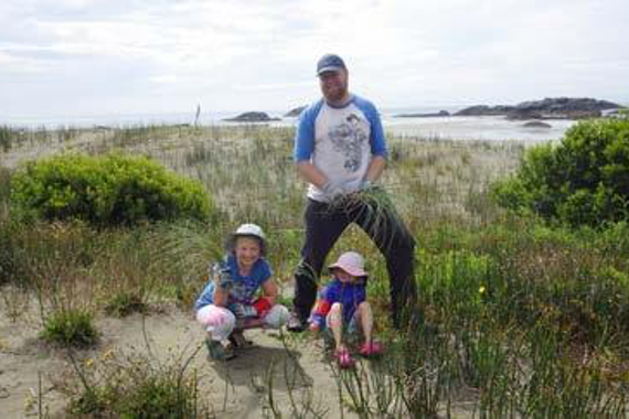 Un homme et deux enfants sur les dunes d’une plage.