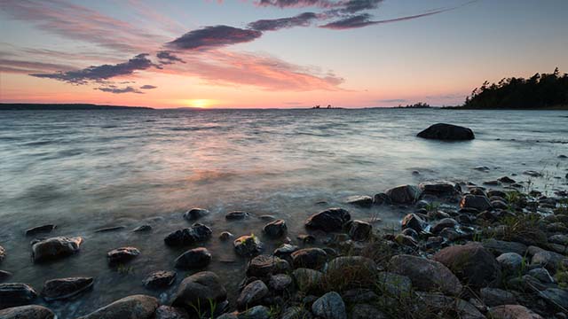 Coucher de soleil sur un lac calme avec un rivage rocheux.