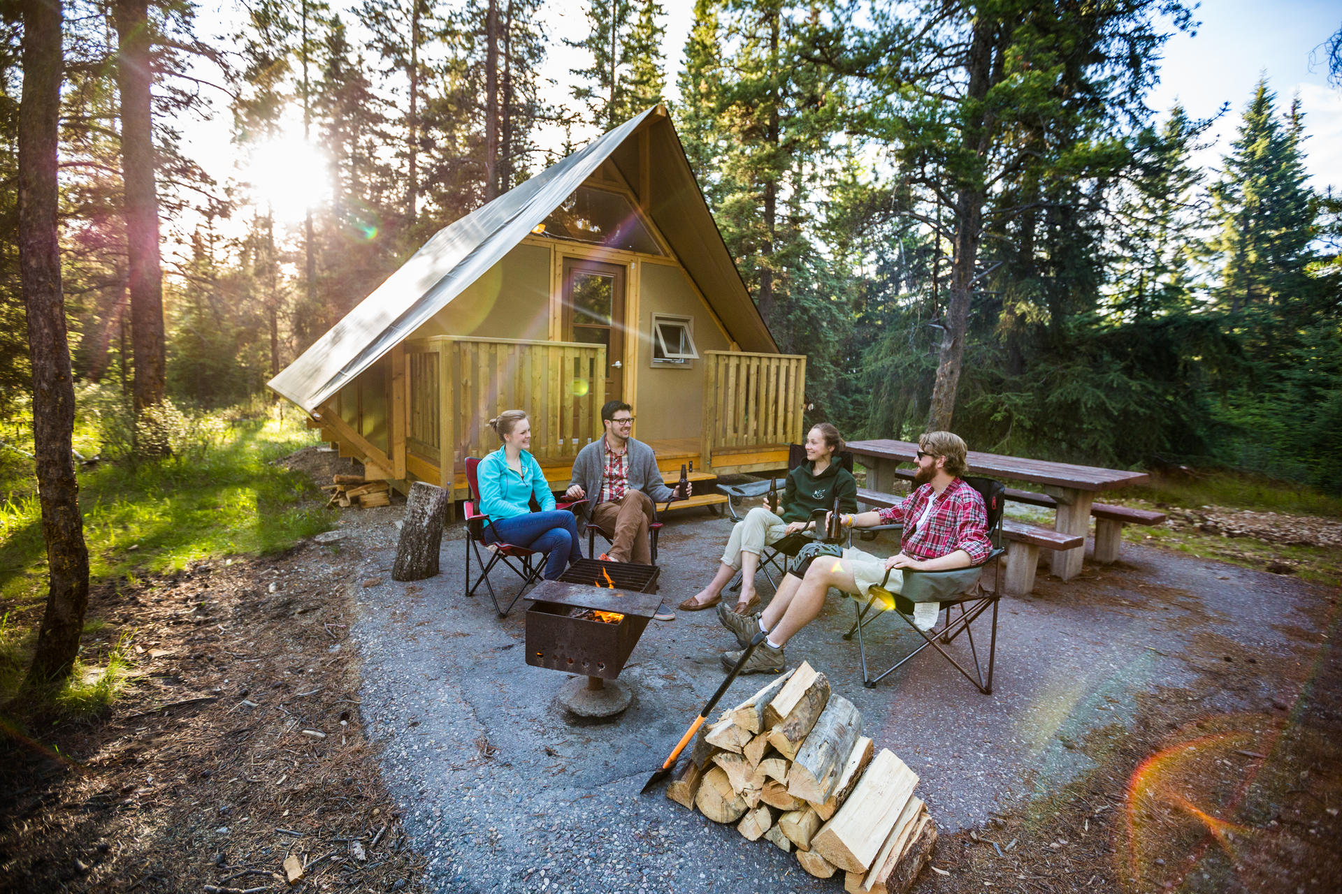 A group of young adults around a campfire beside an oTENTIK at Whistlers Campground, in Jasper National Park.