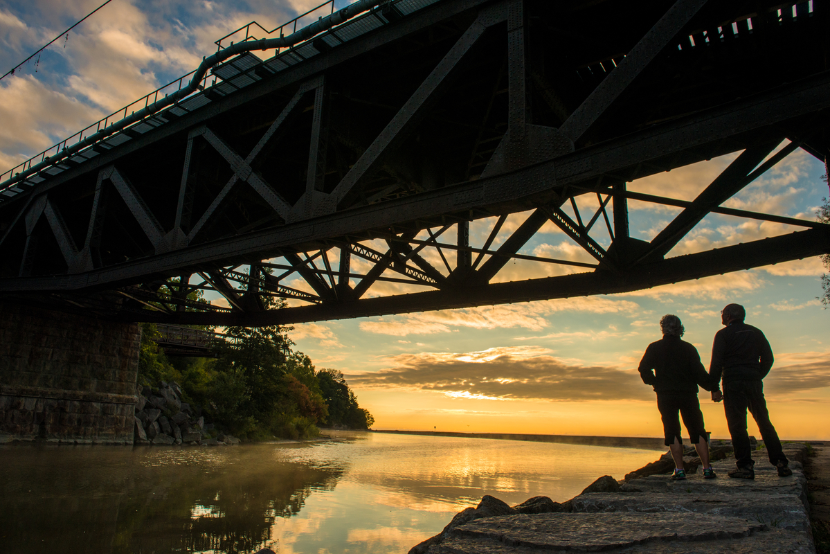 Two people standing underneath a bridge at Rouge Beach at sunset.