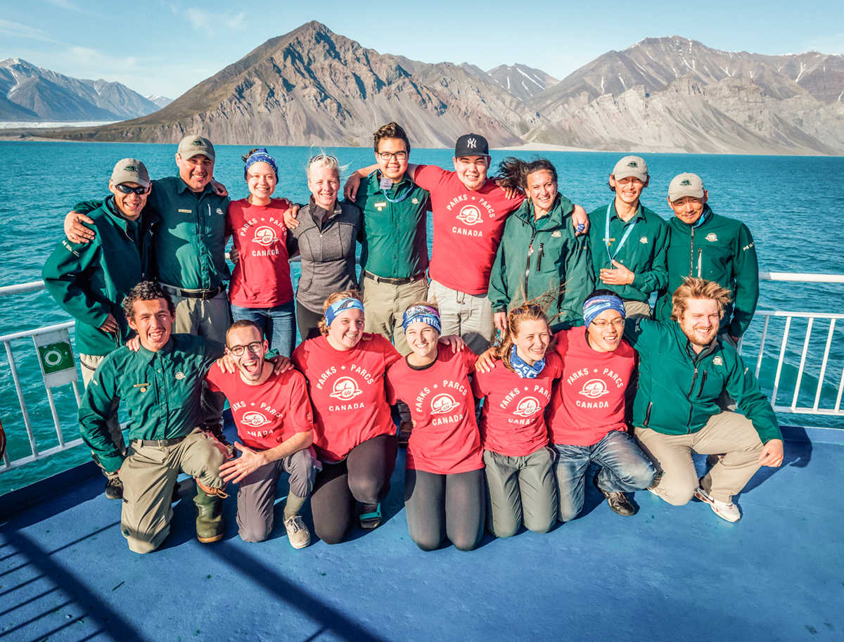 La ministre McKenna et un groupe d’étudiants posent pour une photo de groupe sur le pont d’un navire devant un paysage de mer et de montagnes au Nunavut. 