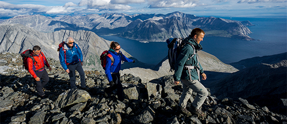 Un employé de Parcs Canada accompagne 3 visiteurs en randonnée pédestre, des montagnes en arrière-plan.