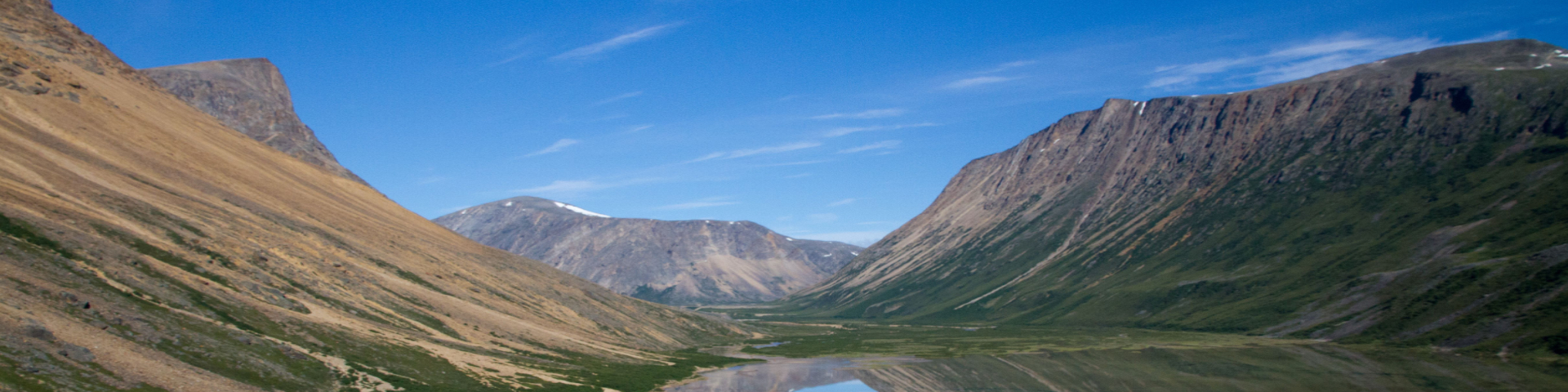 Un fjord d'un bleu profond niché entre d'imposantes montagnes vertes et brunes au loin.