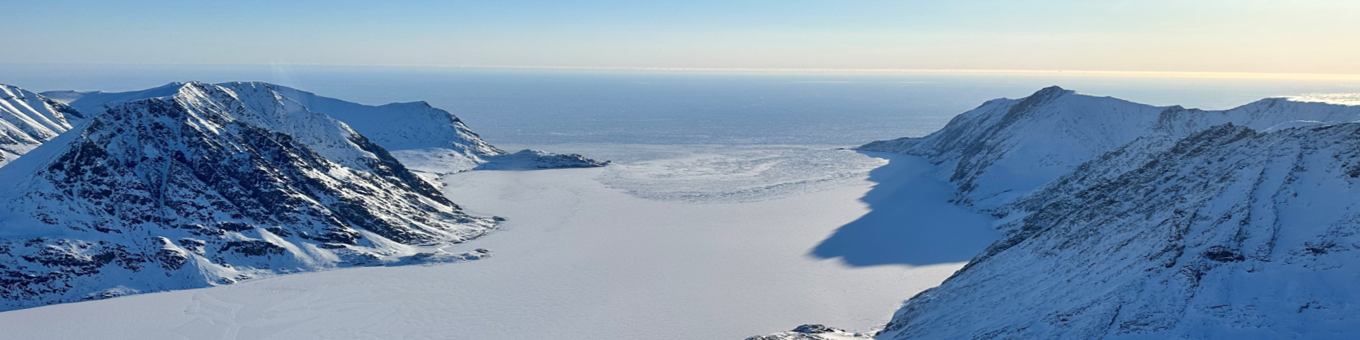 An aerial view of a large, snow covered frozen bay surrounded by snow-capped mountains.