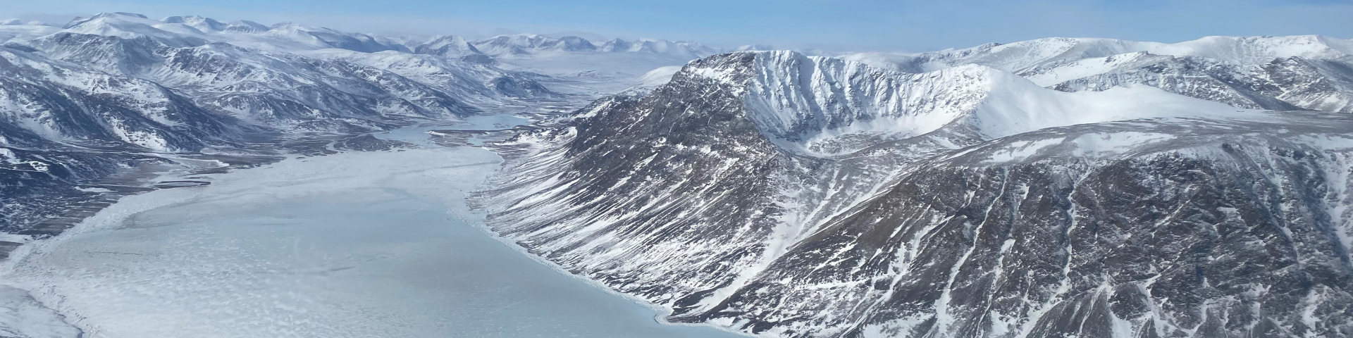 An aerial view of a large, snow covered frozen bay surrounded by snow-capped mountains.