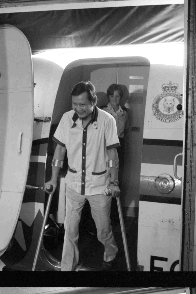 Photo en noir et blanc d’un adulte utilisant des béquilles sortant d’un avion