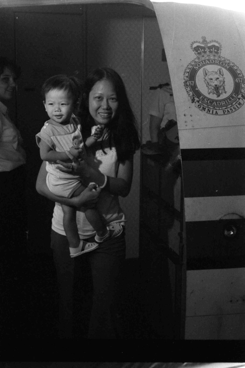 Photo en noir et blanc d’un adulte tenant un enfant dans ses bras et sortant d’un avion
