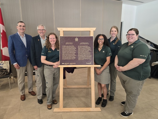 Group of people standing beside a bronze commemorative plaque in an indoor setting