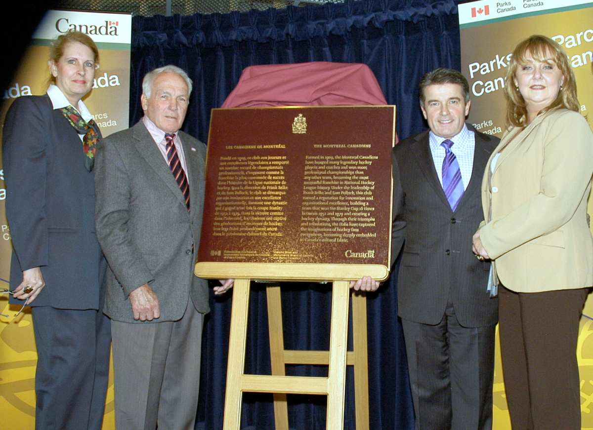 Four persons standing beside commemorative plaque for Club de hockey Canadien National Historic Event