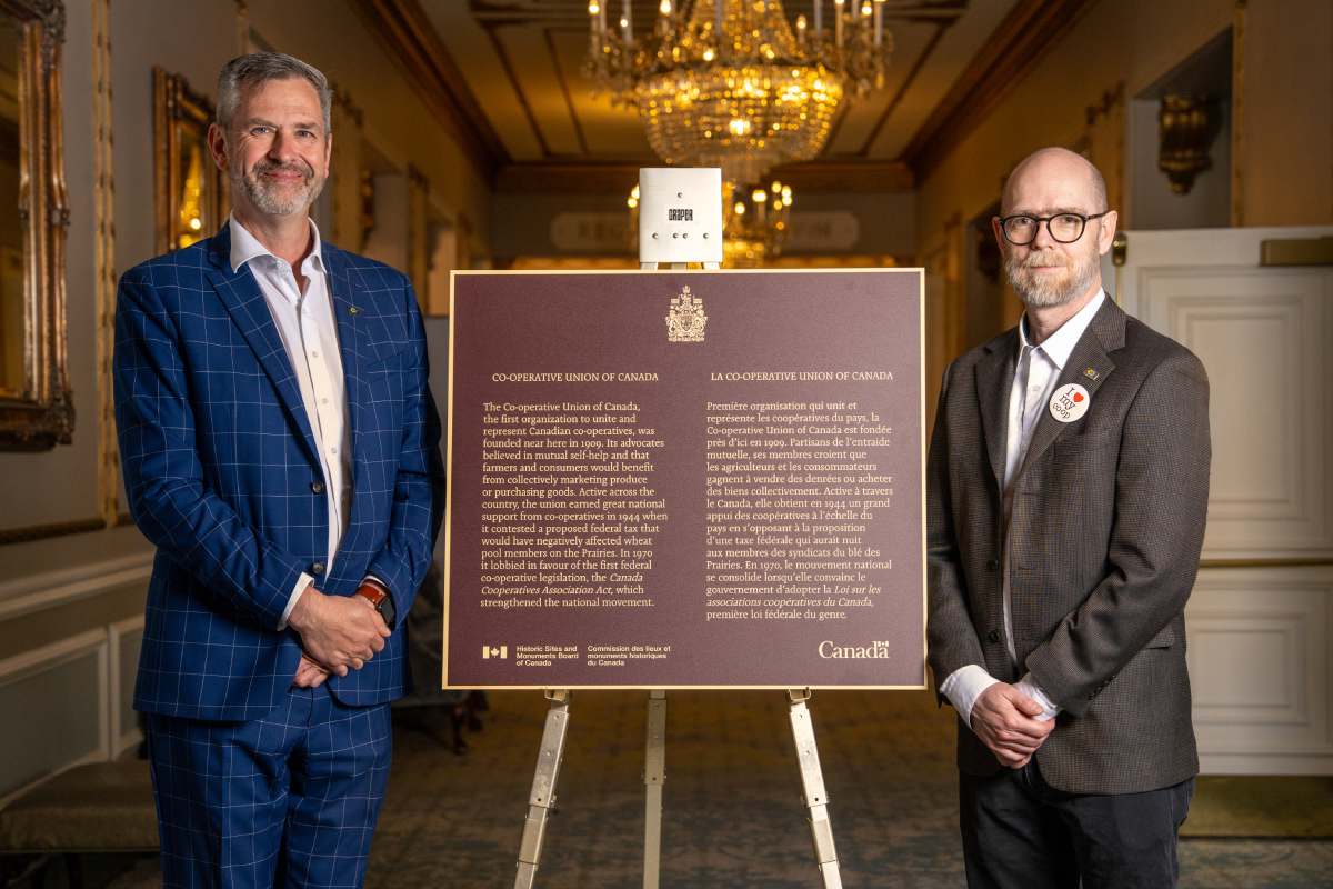 Two members of Cooperatives and Mutuals Canada near a commemorative plaque for the historical importance of the Co-operative Union of Canada National Historic Event 