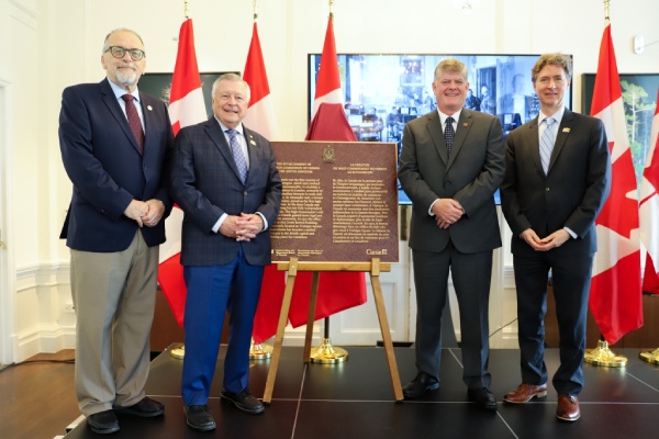 Four persons stand proudly beside a recently unveiled commemorative plaque for the Establishment of the High Commission of Canada in the United Kingdom National Historic Event