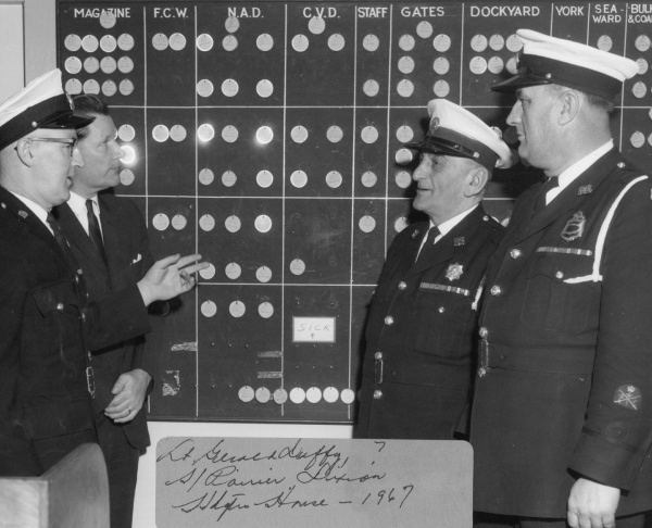 Members of the Canadian Corps of Commissionaires deliberating in front of an assignment board, Nova Scotia, 1967