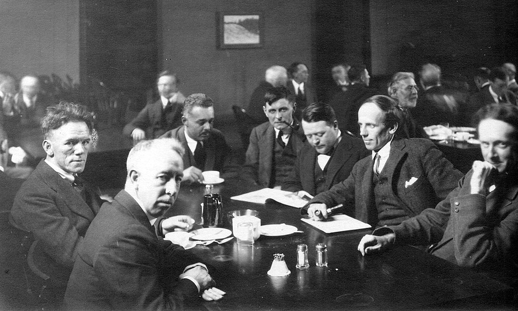Black and white photo of a group of man seated at a table in a public space
