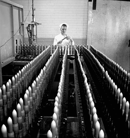 Female worker removes masks placed on shells prior to painting them at Defence Industries Limited, 1944