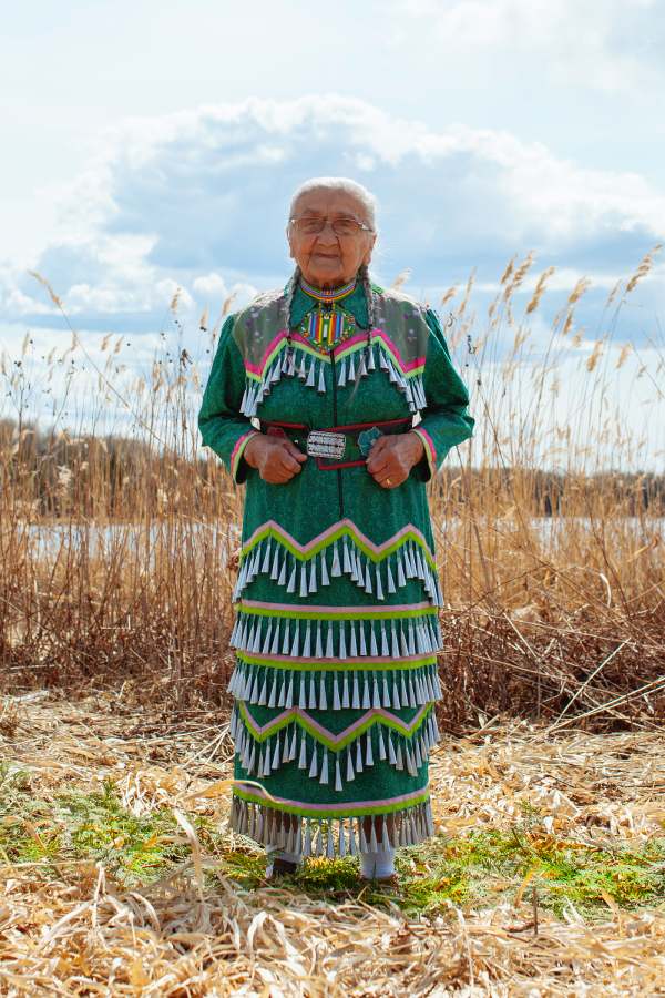 A lady wearing a colorful jingle dress in an outdoor setting