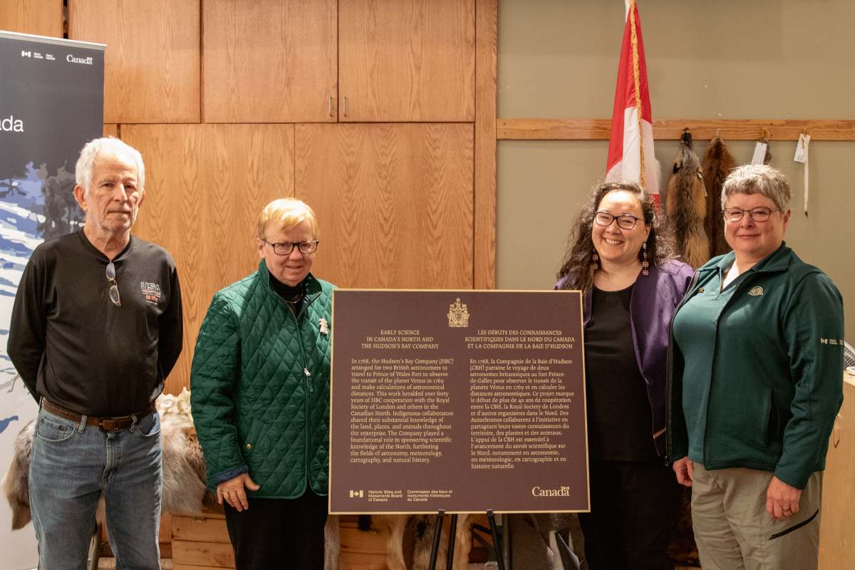Quatre personnes se tiennent à côté d'une plaque commémorative dévoilée dans un espace intérieur