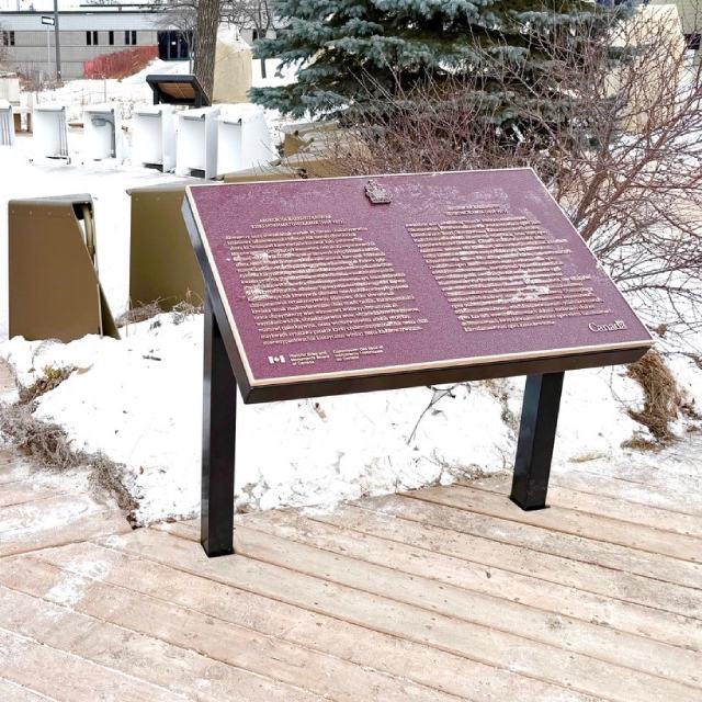A commemorative plaque for Assiniboia Residential School (1958–1973) is installed in a wooden walkpath in a town