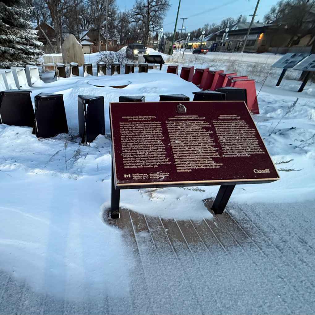 A commemorative plaque for Assiniboia Residential School (1958–1973) is installed on a wooden path